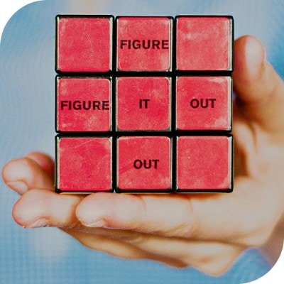 Hand, die einen Zauberwürfel (Rubik's Cube) hält. Auf dem Würfel ist waagerecht und senkrecht der Satz "Figure it out" aufgedruckt.